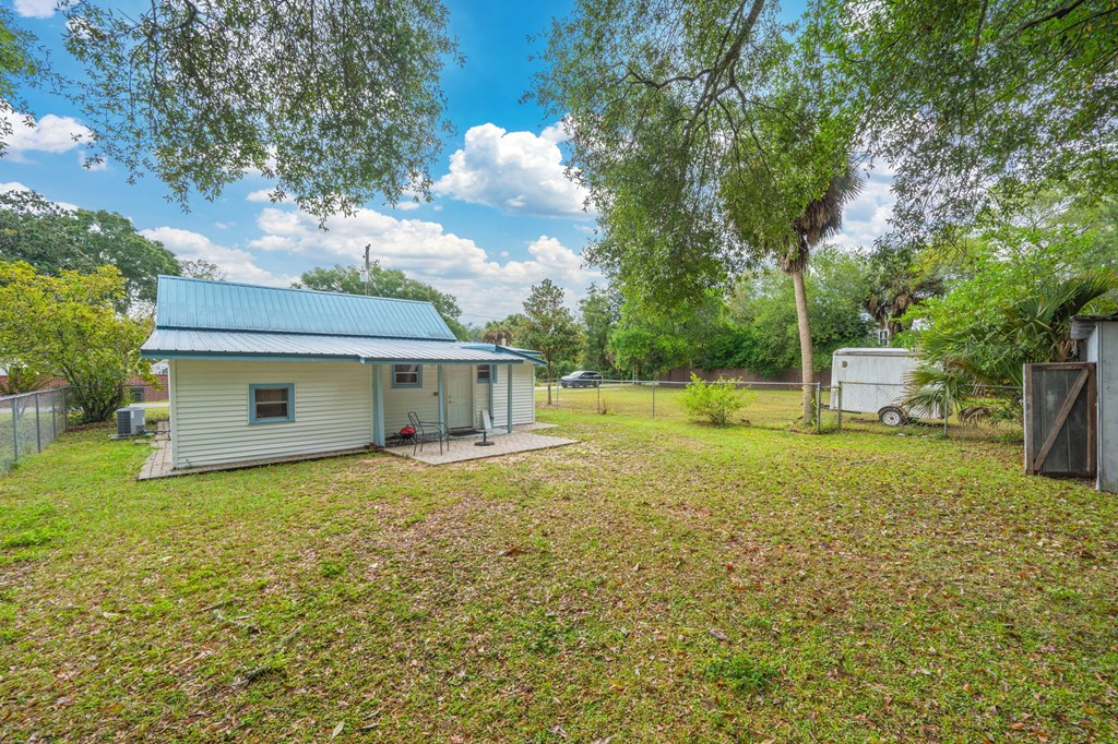 A small house with a metal roof is surrounded by a grassy area with trees.