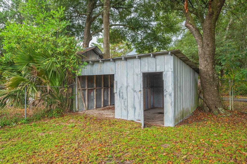 A small, old, grey shack with a door open in the middle of a grassy area.