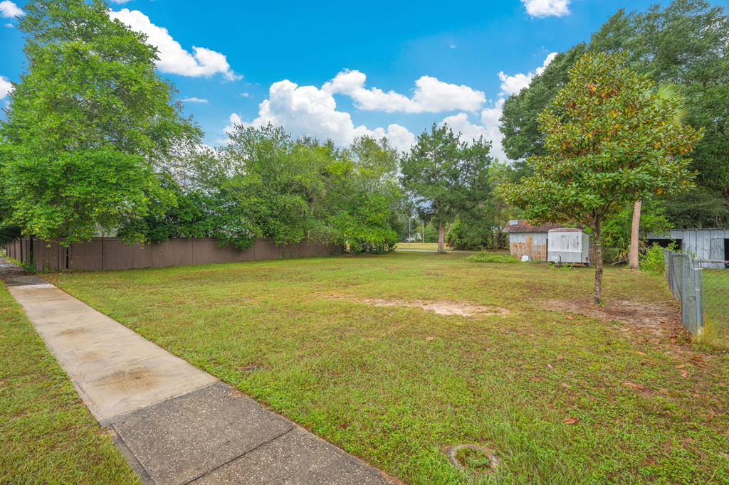 A backyard with a concrete walkway and a fence.