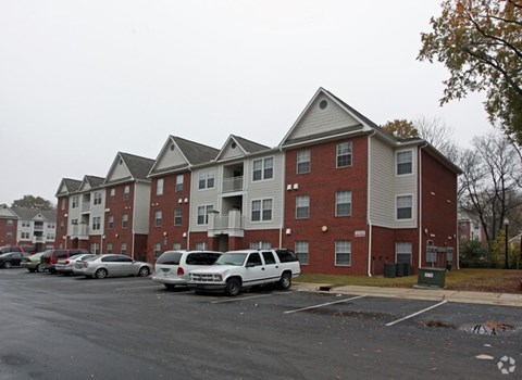 A white car is parked in a parking lot in front of a red brick apartment building.