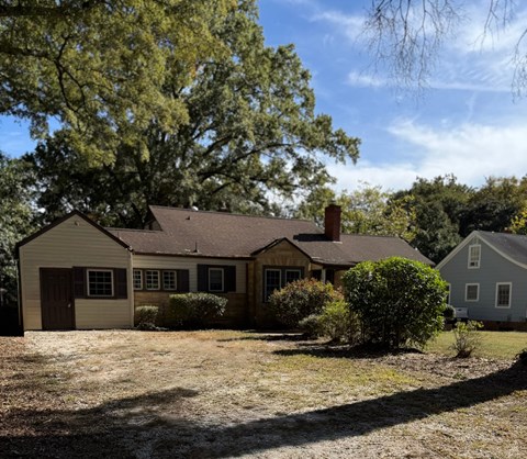 A house with a brown roof and a white garage door is surrounded by trees.