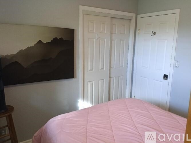 A bedroom with a pink bedspread and a painting on the wall.