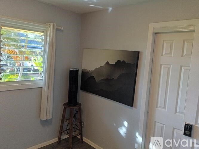 A room with a painting of a mountain on the wall and a speaker on a stool.