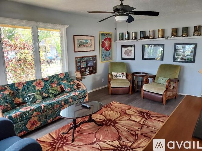 A living room with a floral sofa, two armchairs, a coffee table, and a ceiling fan.