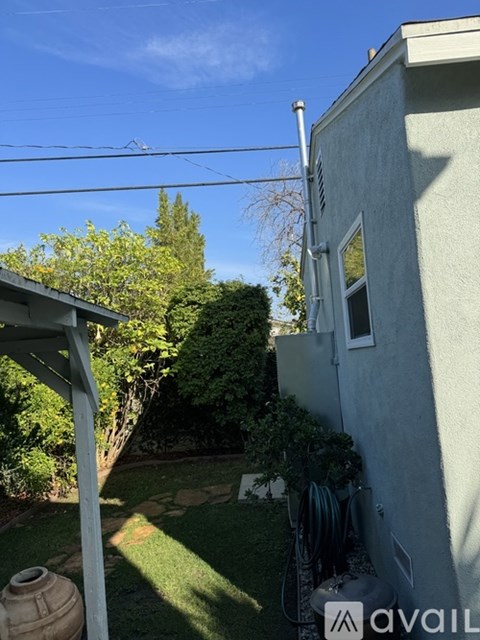 A house with a grey wall and a white door is surrounded by greenery.