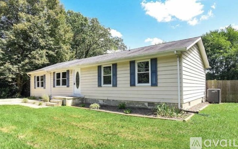 A small house with a porch and a white door is surrounded by a grassy yard.