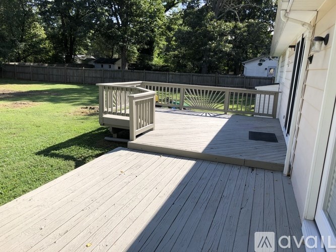 A wooden deck with a railing and a small table is in the foreground of a sunny backyard.