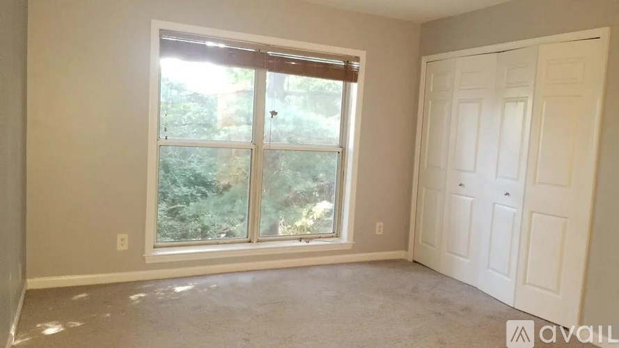 A room with a large window and a white door is available for rent.