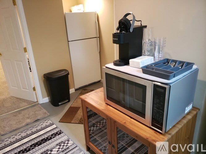 A room with a white fridge, a wooden table with a microwave and a speaker on it, and a rug on the floor.