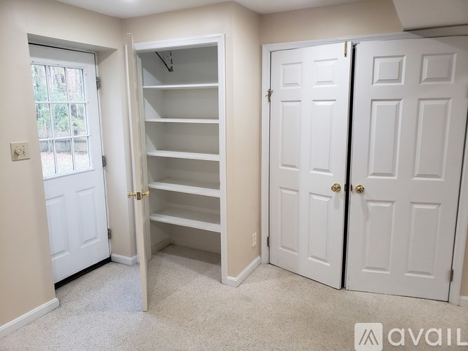 A room with a white door, a white shelving unit, and a white carpet.