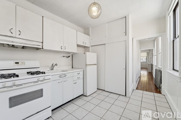 A white kitchen with a stove, sink, and cabinets.
