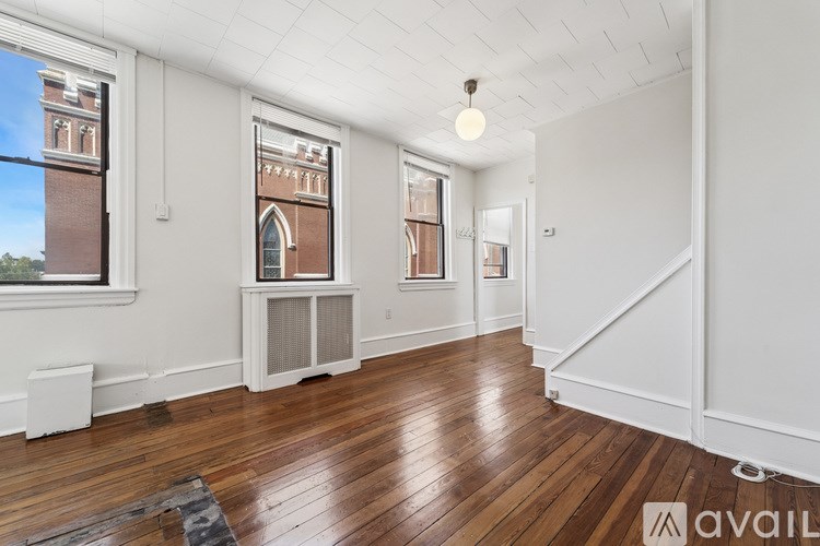 A room with wooden floors and white walls, featuring a window with a view of a brick building and a white radiator.