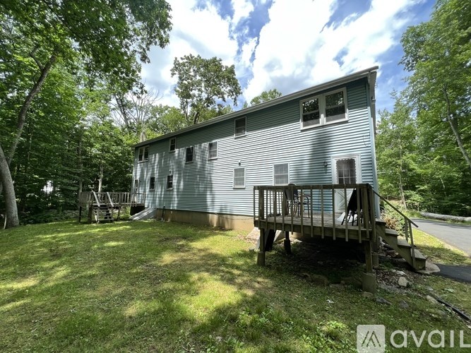 A house with a porch and a deck is surrounded by trees.