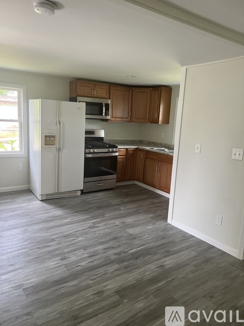 A kitchen with a white fridge, wooden cabinets, and a grey floor.