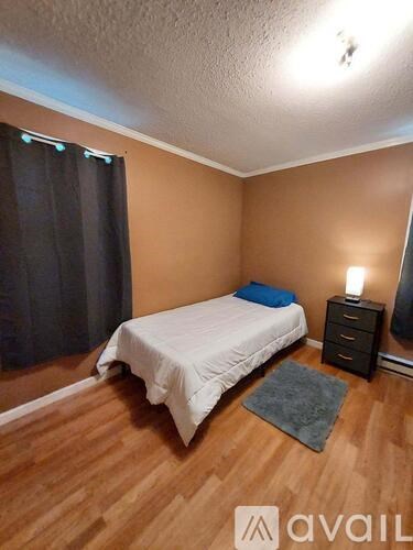 A bedroom with a bed, nightstand, and window with curtains.