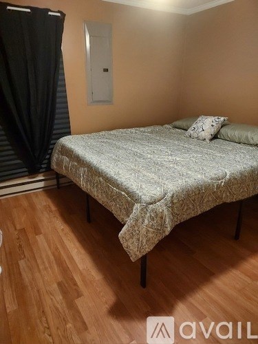A bed with a grey bedspread and two pillows sits in a room with wooden flooring.