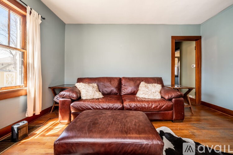A brown leather couch and ottoman in a room with wooden floors and a window.