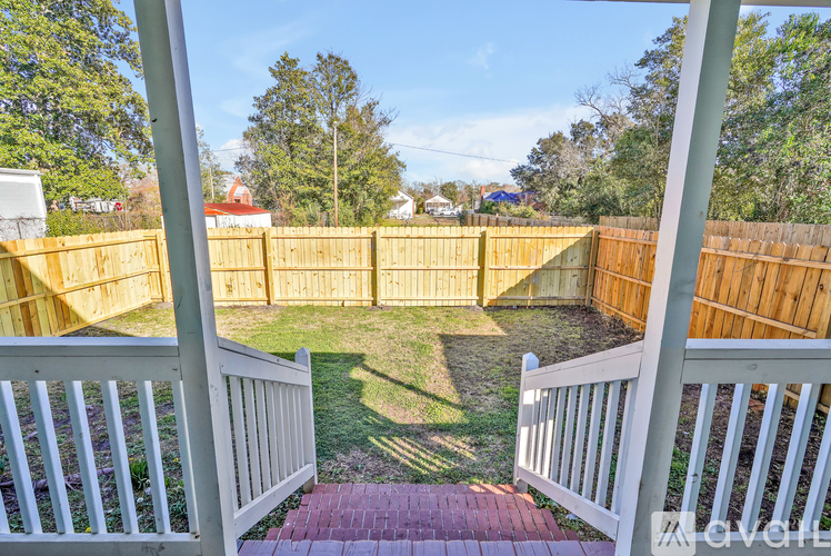 A backyard with a white fence and a brick pathway leading to a grassy area.