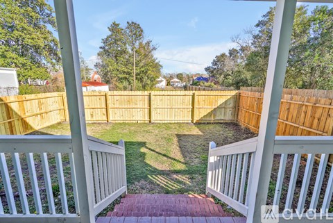 A backyard with a white fence and a brick pathway leading to a grassy area.