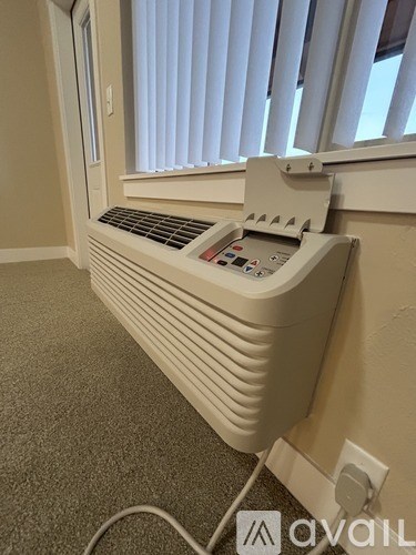 A white electric heater is plugged into a wall socket.