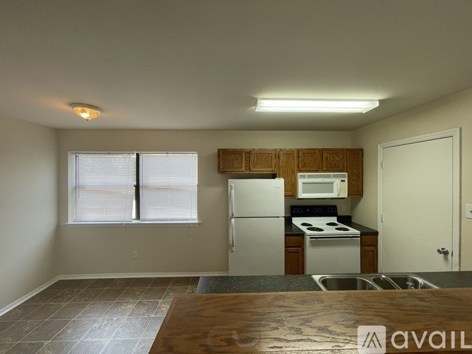 A kitchen with a white refrigerator and stove, wooden cabinets, and a window with blinds.