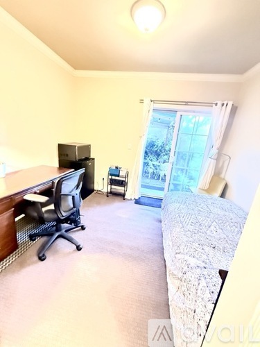 A bed with a black and white patterned comforter sits in a room with a wooden floor and a carpet.