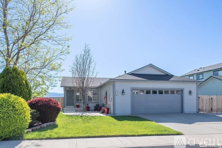 A white house with a grey garage door is surrounded by a green lawn and trees.