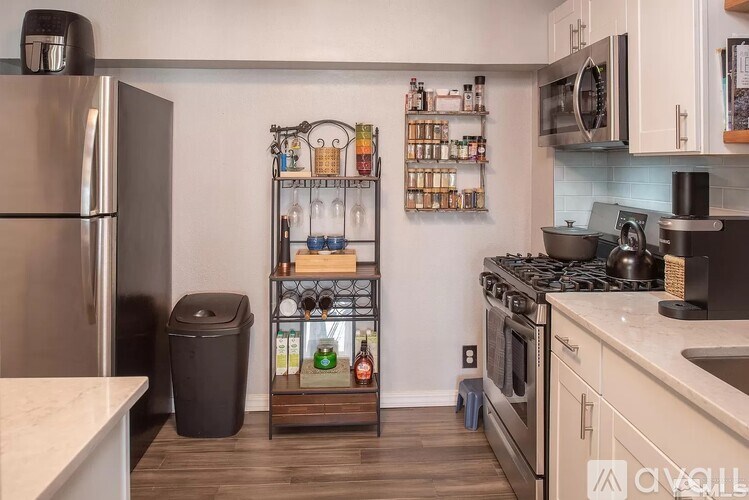 A kitchen with a refrigerator, a shelf with bottles and jars, and a stove top oven.