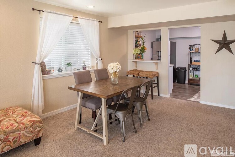 A dining room with a wooden table and chairs, a bench, and a window with curtains.