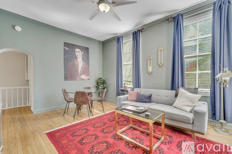 A living room with a grey couch, a red rug, and a ceiling fan.