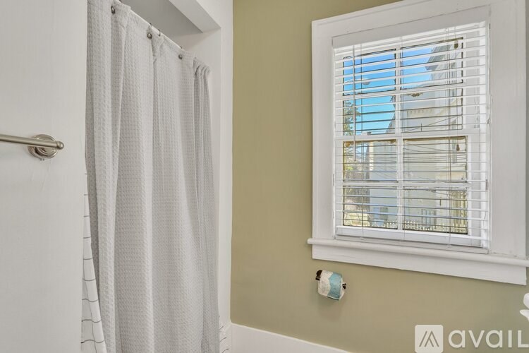 A bathroom with a white shower curtain and a window with blinds.