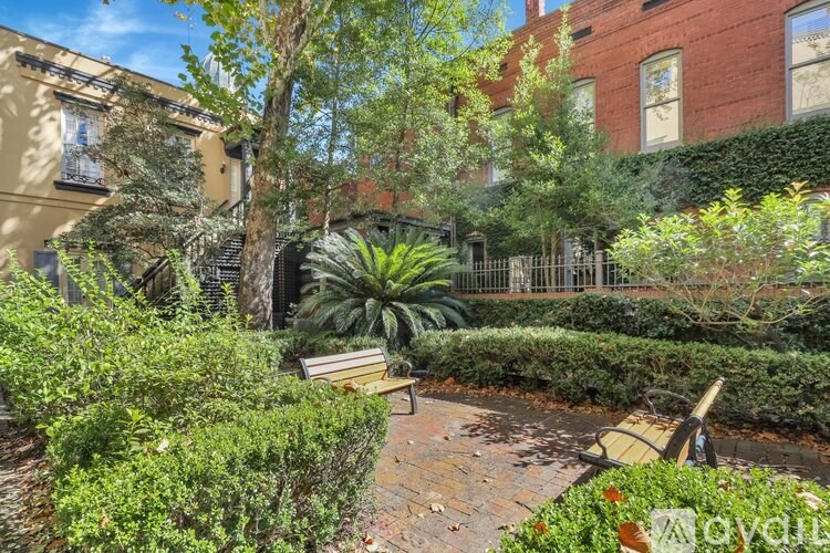A small garden with a bench and a tree in front of a red brick building.