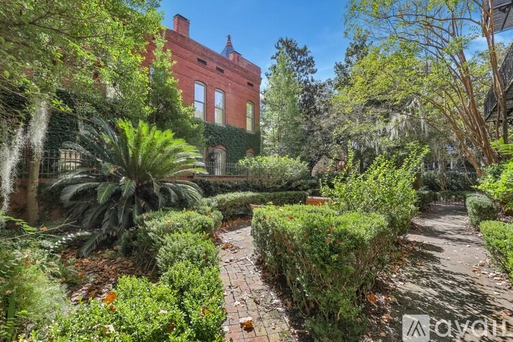 A lush garden with a brick pathway leading to a red brick building.