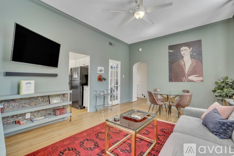A living room with a grey couch, a red rug, and a television on the wall.