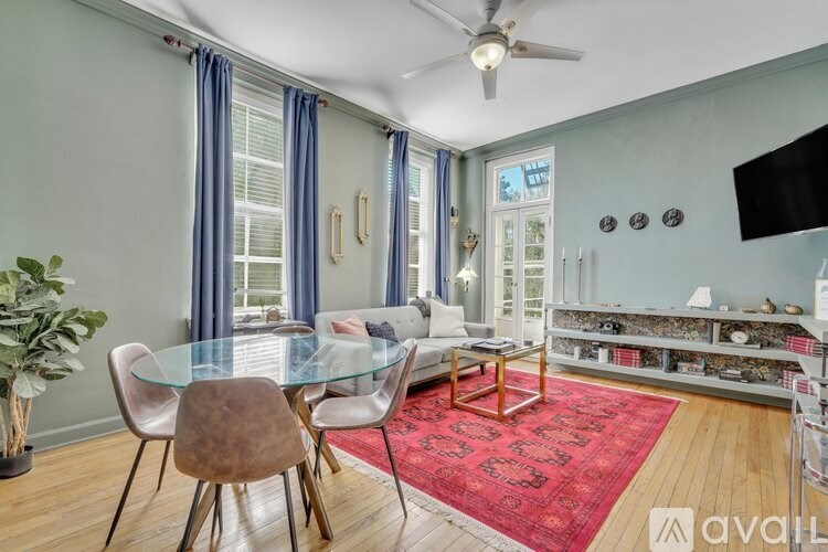 A living room with a glass table and chairs, a red rug, and a ceiling fan.