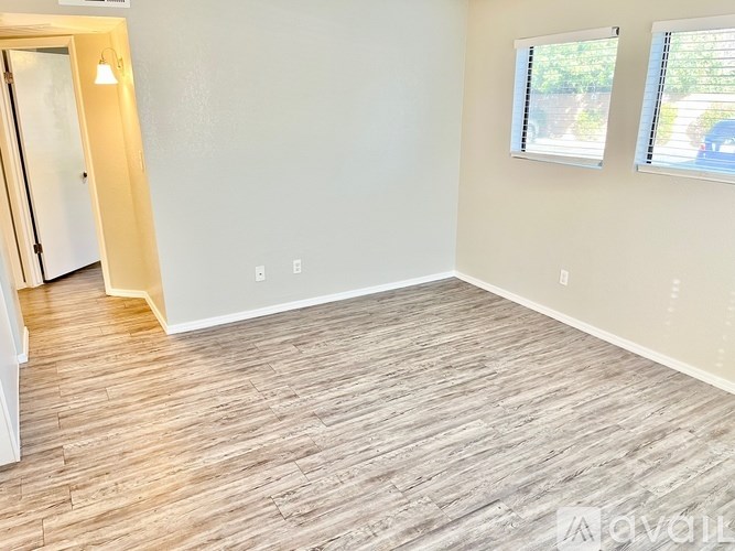 A room with wooden flooring and two windows.