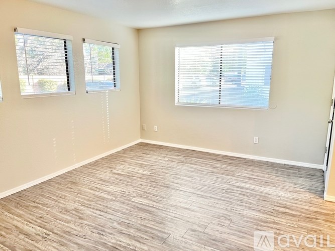 A room with light brown flooring and two windows with blinds.