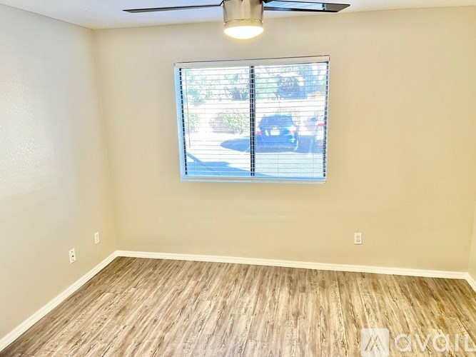 A room with a ceiling fan and a window showing a street view.
