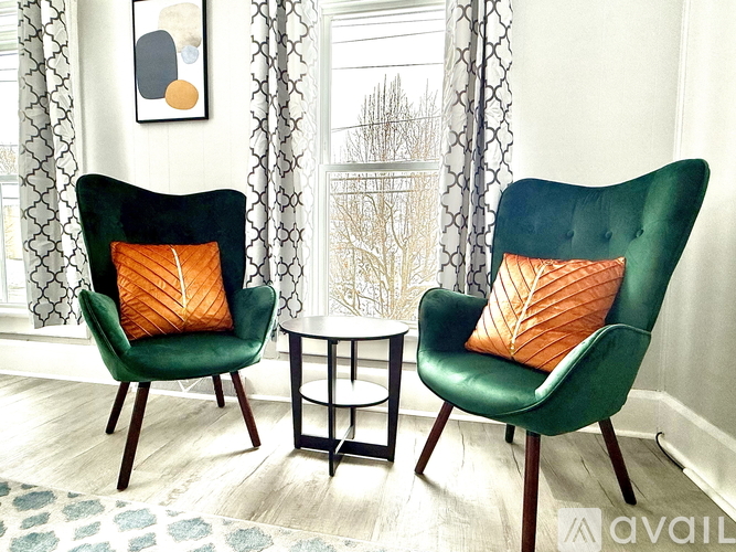 Two green chairs with orange pillows in front of a window.