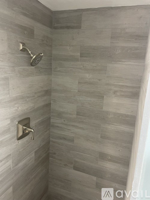 A shower with a wall of tiles and a wall-mounted shower head.