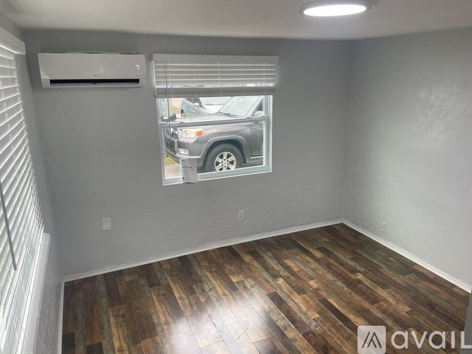 A room with wooden flooring and a window showing a car outside.