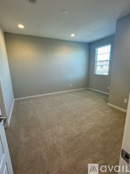 A room with beige carpeting and a window with blinds.