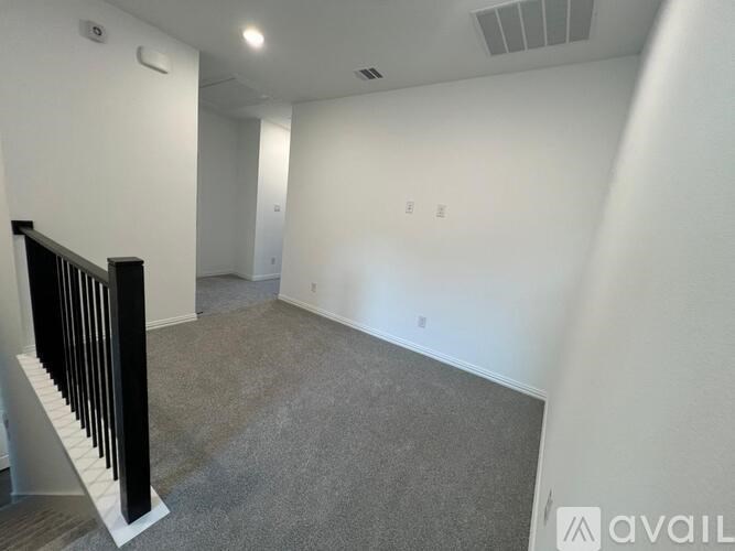 A spacious room with a carpeted floor and a staircase on the left side.