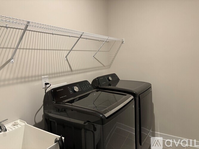 A black washing machine sits in front of a wire shelf.