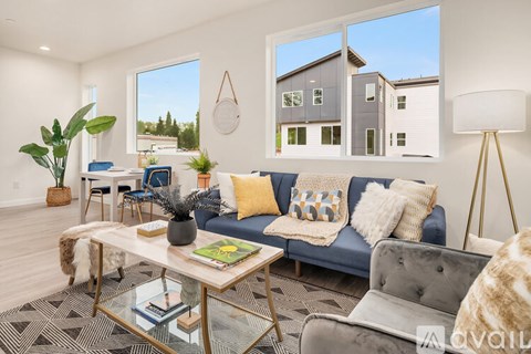 A modern living room with a grey couch, a glass coffee table, and a large window.
