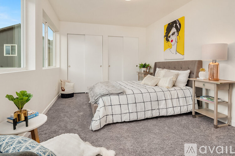 A bedroom with a bed, nightstand, and a painting of a woman's face on the wall.