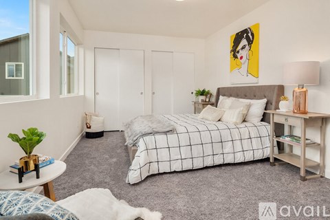 A bedroom with a bed, nightstand, and a painting of a woman's face on the wall.