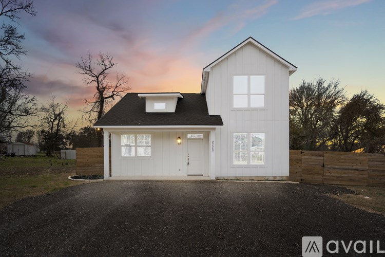 A house with a white exterior and a black roof is shown with a gravel driveway in front.