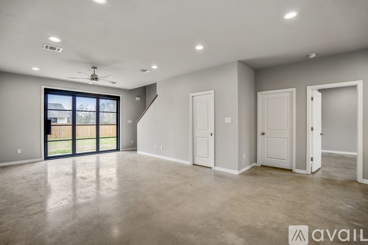 A spacious room with a ceiling fan and a large window with a view of a fence and trees.