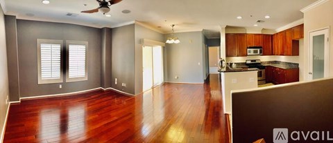 A spacious living room with hardwood floors and a kitchen area in the background.